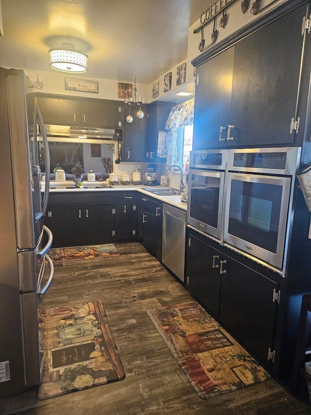 kitchen with stainless steel appliances, a sink, dark cabinetry, light countertops, and dark wood-type flooring