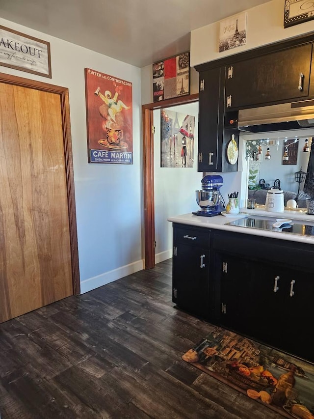 kitchen featuring dark cabinetry, light countertops, baseboards, and dark wood-style flooring