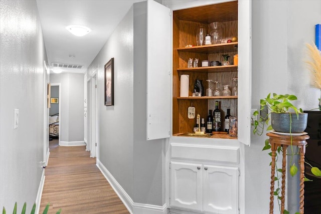 corridor featuring light wood finished floors, visible vents, and baseboards