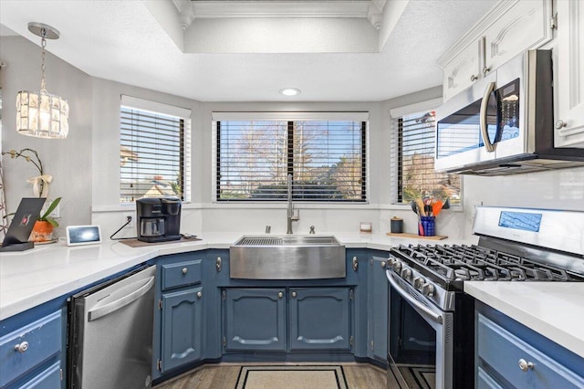 kitchen with pendant lighting, light countertops, appliances with stainless steel finishes, a sink, and blue cabinets