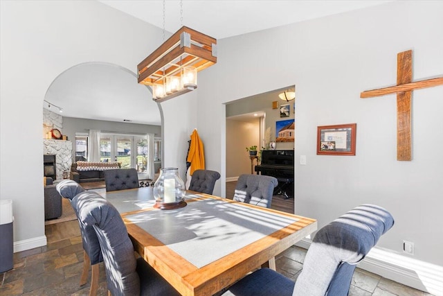 dining area featuring stone tile floors, baseboards, arched walkways, a stone fireplace, and a chandelier