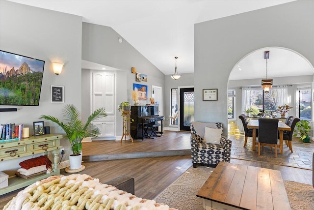 living room featuring baseboards, high vaulted ceiling, arched walkways, and wood finished floors