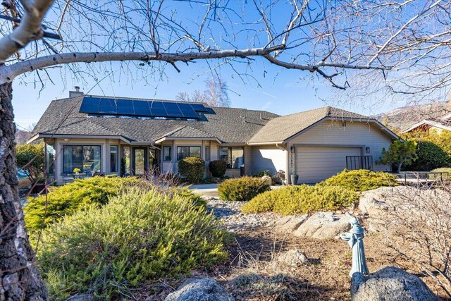 ranch-style house with roof mounted solar panels, a chimney, and an attached garage