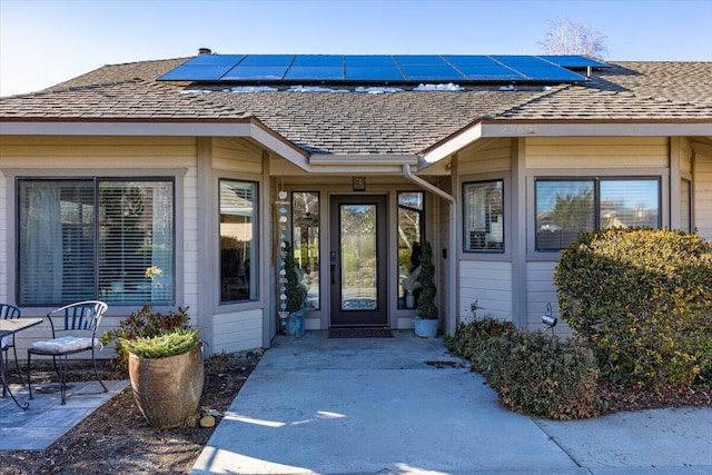 entrance to property with roof with shingles and roof mounted solar panels