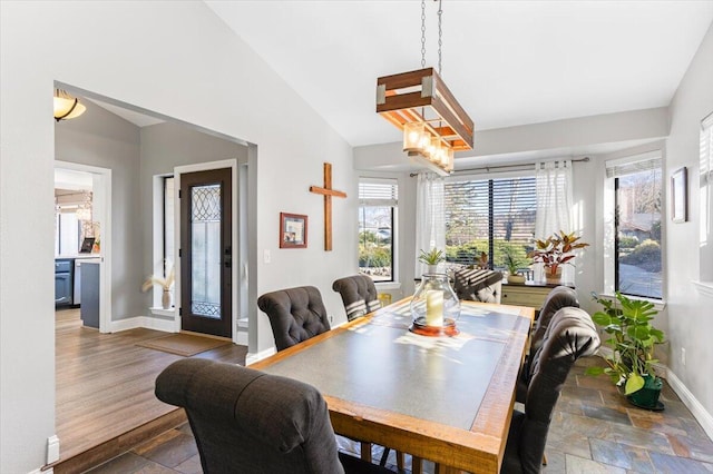 dining space with a healthy amount of sunlight, stone tile floors, baseboards, and vaulted ceiling