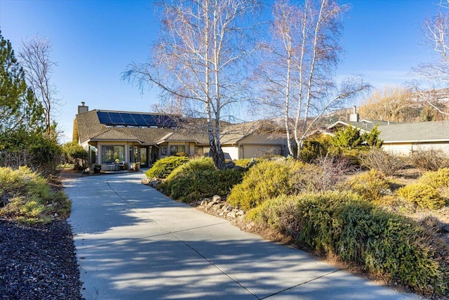 view of front of property featuring concrete driveway, a chimney, an attached garage, and solar panels