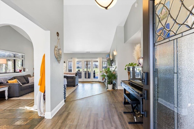 foyer entrance featuring baseboards, arched walkways, a towering ceiling, wood finished floors, and french doors