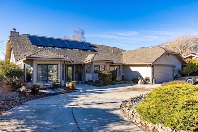 single story home featuring a shingled roof, concrete driveway, an attached garage, and solar panels