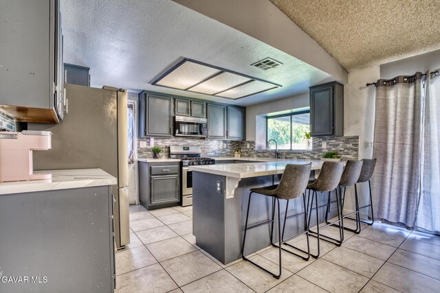 1027 James Ct, Lancaster, CA 93535 - kitchen with stainless steel appliances, a peninsula, a textured ceiling, light countertops, and light tile patterned floors