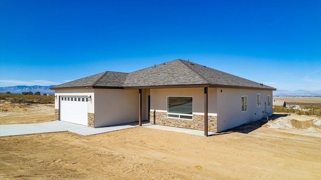 view of front of house featuring an attached garage, stone siding, a mountain view, and stucco siding