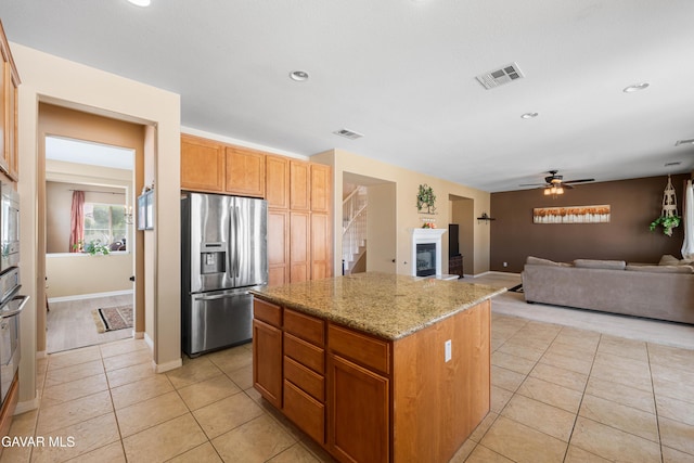41507 Alexo Dr, Lancaster, CA 93536 - kitchen featuring stainless steel appliances, a kitchen island, light tile patterned floors, light stone counters, and a glass covered fireplace