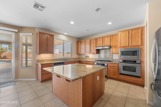 41507 Alexo Dr, Lancaster, CA 93536 - kitchen with appliances with stainless steel finishes, a center island, under cabinet range hood, light stone countertops, and tasteful backsplash
