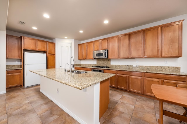 kitchen featuring appliances with stainless steel finishes, sink, backsplash, light stone counters, and a center island with sink