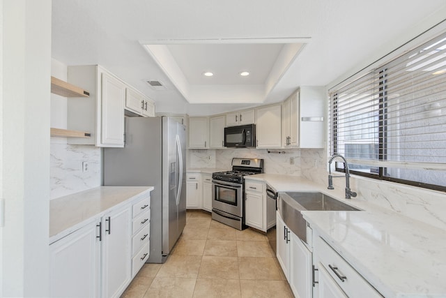 kitchen featuring visible vents, a raised ceiling, appliances with stainless steel finishes, open shelves, and a sink