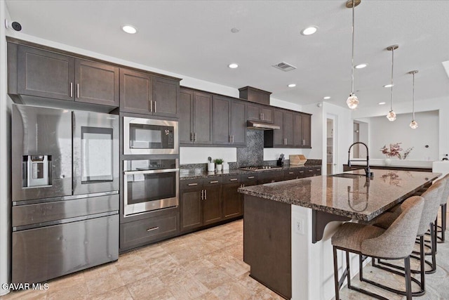 39057 Mondell Pine Ave, Palmdale, CA 93551 - kitchen with stainless steel appliances, dark brown cabinetry, a kitchen bar, dark stone counters, and a kitchen island with sink