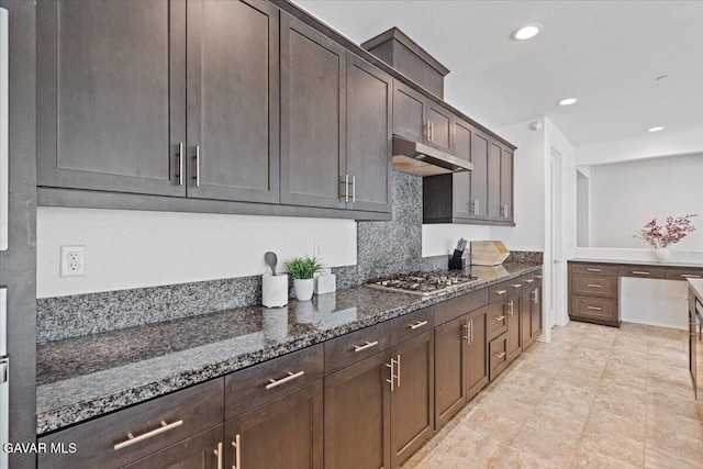 39057 Mondell Pine Ave, Palmdale, CA 93551 - kitchen with under cabinet range hood, stainless steel gas stovetop, dark stone counters, dark brown cabinetry, and tasteful backsplash