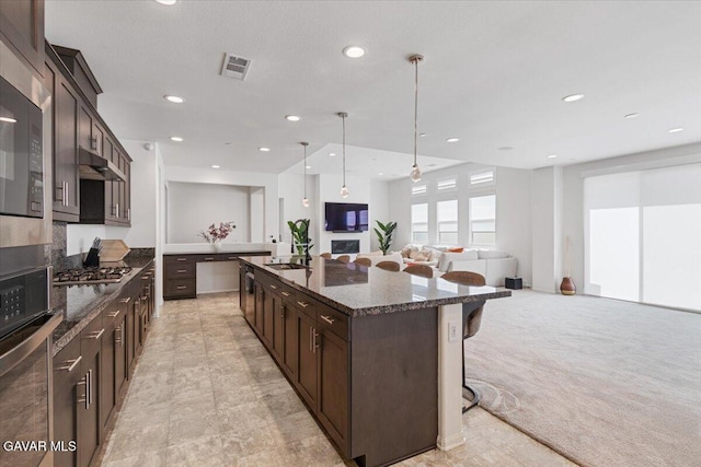 39057 Mondell Pine Ave, Palmdale, CA 93551 - kitchen featuring a breakfast bar, dark brown cabinets, appliances with stainless steel finishes, an island with sink, and dark stone countertops
