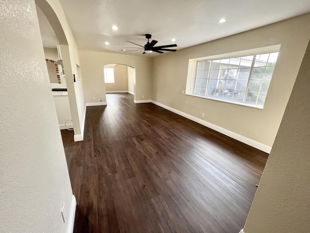 unfurnished living room with ceiling fan, dark wood-type flooring, and plenty of natural light