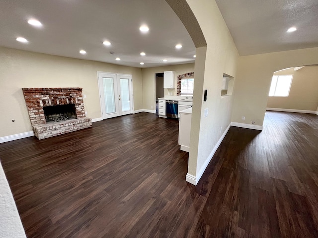 unfurnished living room featuring a healthy amount of sunlight, dark wood-type flooring, and a brick fireplace