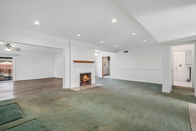 unfurnished living room with dark carpet, a fireplace, and ceiling fan