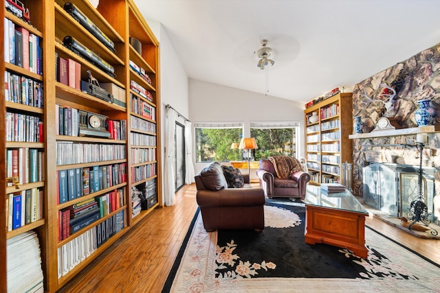 sitting room featuring a stone fireplace, ceiling fan, hardwood / wood-style floors, and vaulted ceiling