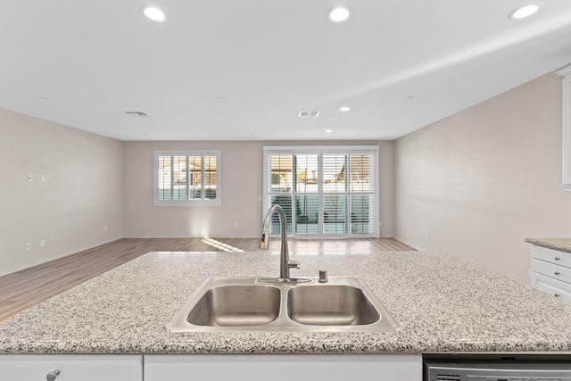 kitchen featuring white cabinets, dishwasher, an island with sink, sink, and light hardwood / wood-style flooring