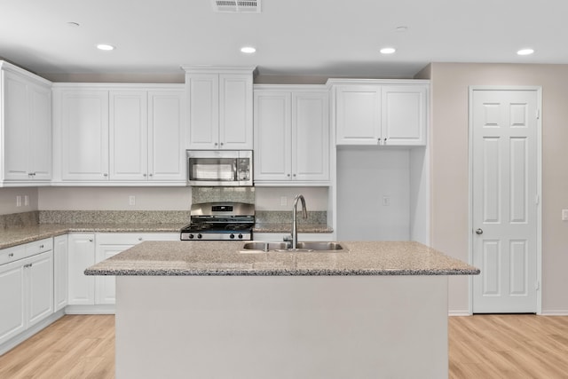 kitchen featuring stove, sink, white cabinetry, light stone countertops, and an island with sink