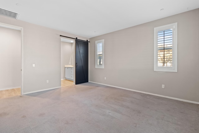 unfurnished bedroom with connected bathroom, light carpet, and a barn door