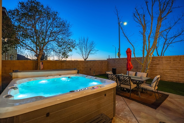 pool at dusk with a patio, outdoor dining area, a fenced backyard, and a hot tub