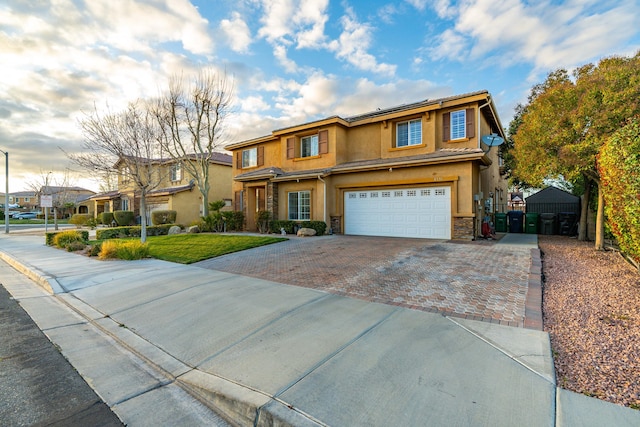 view of front facade with an attached garage, stucco siding, stone siding, driveway, and a gate