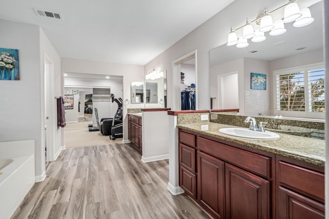 full bath featuring visible vents, a walk in closet, two vanities, wood finished floors, and a sink