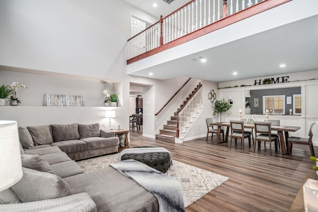 living area featuring stairway, wood finished floors, baseboards, a high ceiling, and recessed lighting