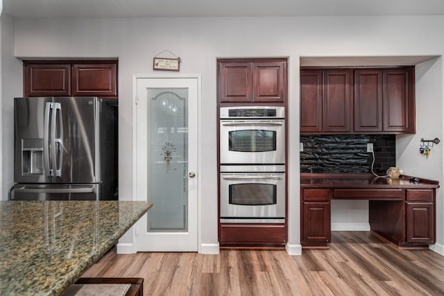 kitchen with light wood-style flooring, backsplash, stainless steel appliances, dark stone counters, and baseboards