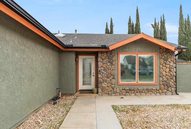 view of exterior entry featuring stucco siding and roof with shingles