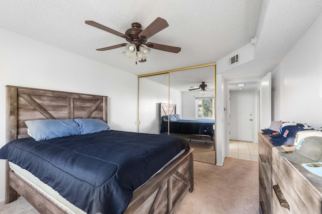 bedroom featuring a textured ceiling, light colored carpet, a closet, and ceiling fan