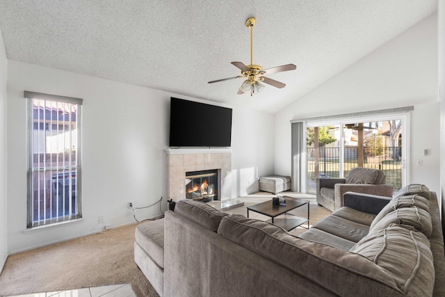 living room featuring light colored carpet, vaulted ceiling, a textured ceiling, a tile fireplace, and ceiling fan