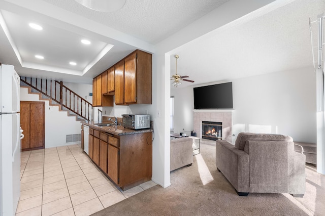 kitchen featuring sink, light tile patterned floors, white appliances, a tile fireplace, and ceiling fan