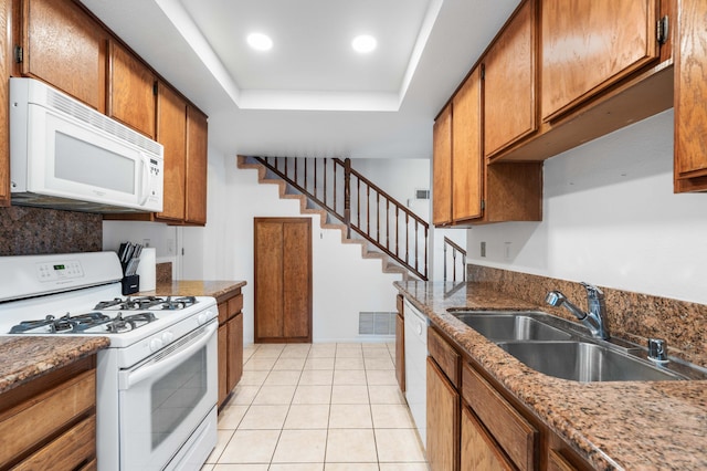 kitchen with sink, white appliances, light tile patterned floors, a raised ceiling, and dark stone counters