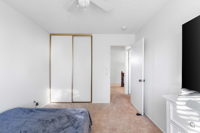 carpeted bedroom with ceiling fan, a closet, and a textured ceiling