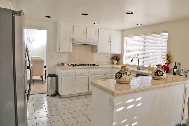 kitchen featuring kitchen peninsula, stainless steel appliances, light tile patterned floors, white cabinets, and tile counters