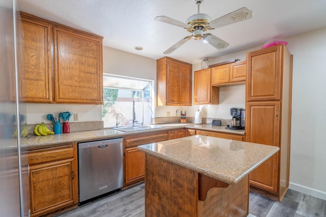 kitchen with a kitchen island, wood-type flooring, sink, stainless steel dishwasher, and light stone counters