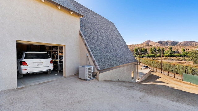 view of property exterior featuring a mountain view, a garage, and central air condition unit