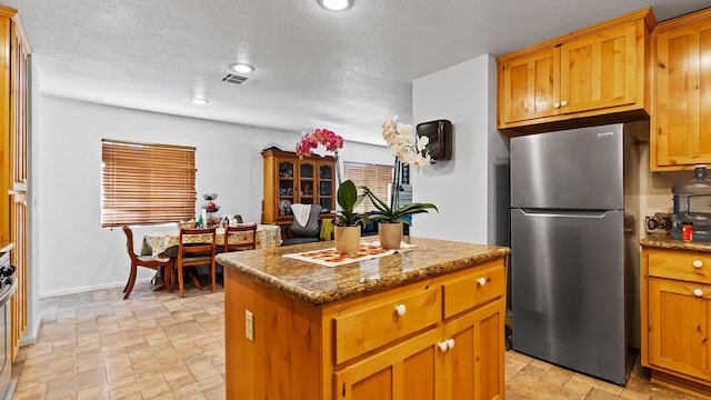 kitchen featuring a kitchen island, a textured ceiling, stainless steel refrigerator, and dark stone counters