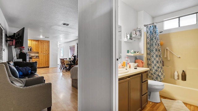 full bathroom featuring a healthy amount of sunlight, shower / bath combo, a textured ceiling, toilet, and vanity