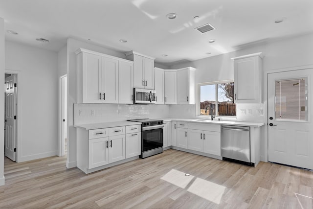 kitchen with white cabinets, light wood-type flooring, stainless steel appliances, and sink