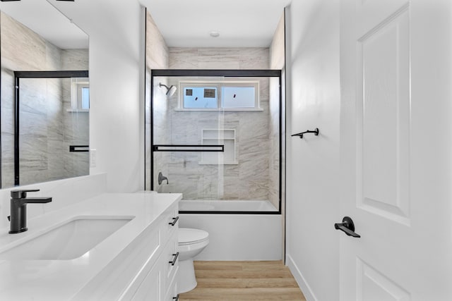 full bathroom featuring hardwood / wood-style floors, toilet, combined bath / shower with glass door, and vanity