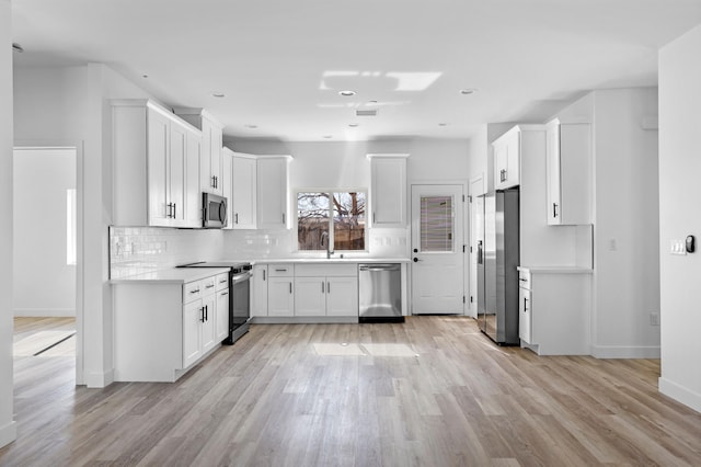 kitchen with white cabinets, appliances with stainless steel finishes, light hardwood / wood-style floors, and decorative backsplash