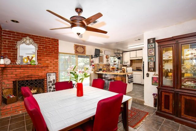 dining room featuring dark tile patterned flooring, ceiling fan, and a fireplace
