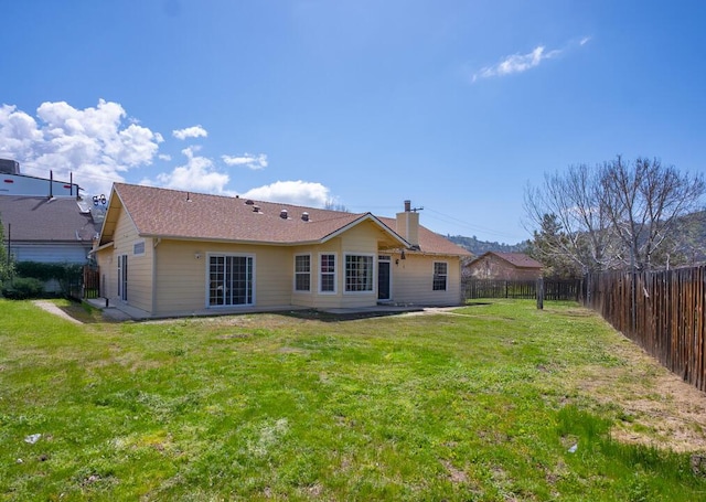 rear view of house with a fenced backyard, a chimney, and a yard
