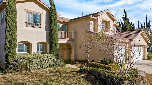 view of front of home with concrete driveway, a tiled roof, a balcony, and stucco siding